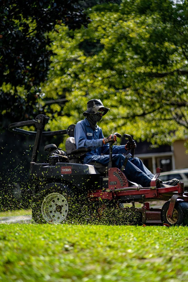 Landscaping worker riding a mower across a green lawn