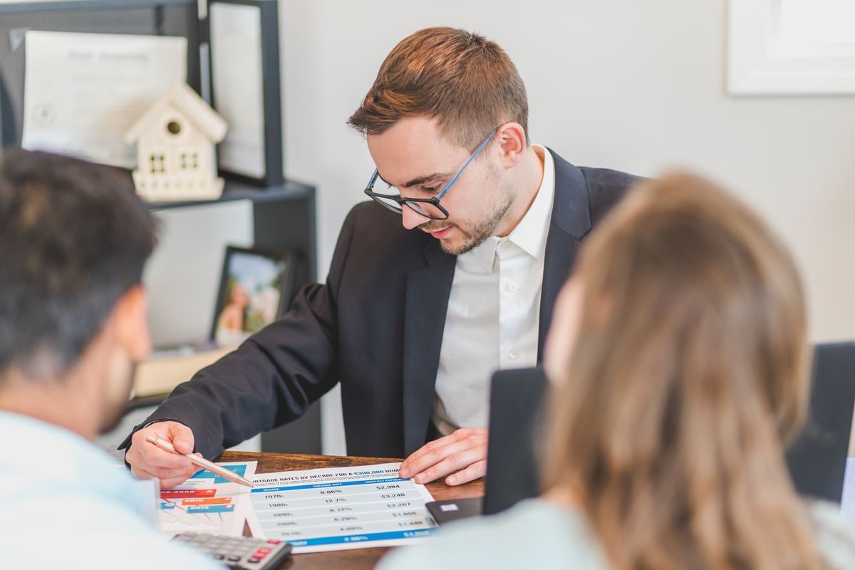 Advisor explaining plan documents to a client couple at a desk with a laptop and calculator