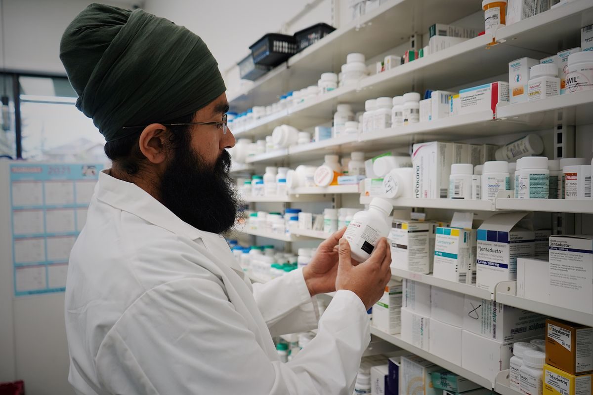 Pharmacist checking a prescription bottle in front of pharmacy shelves